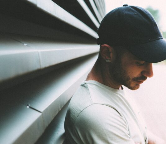 여름철 자외선으로부터 모발 보호법 man wearing black cap and white shirt leaning on gray metal wall