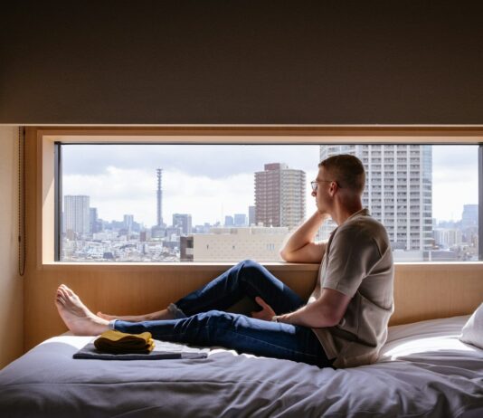 뇌건강, 지금부터 챙겨야 할 이유와 실천법 Man relaxes on a bed, gazing at a city view.