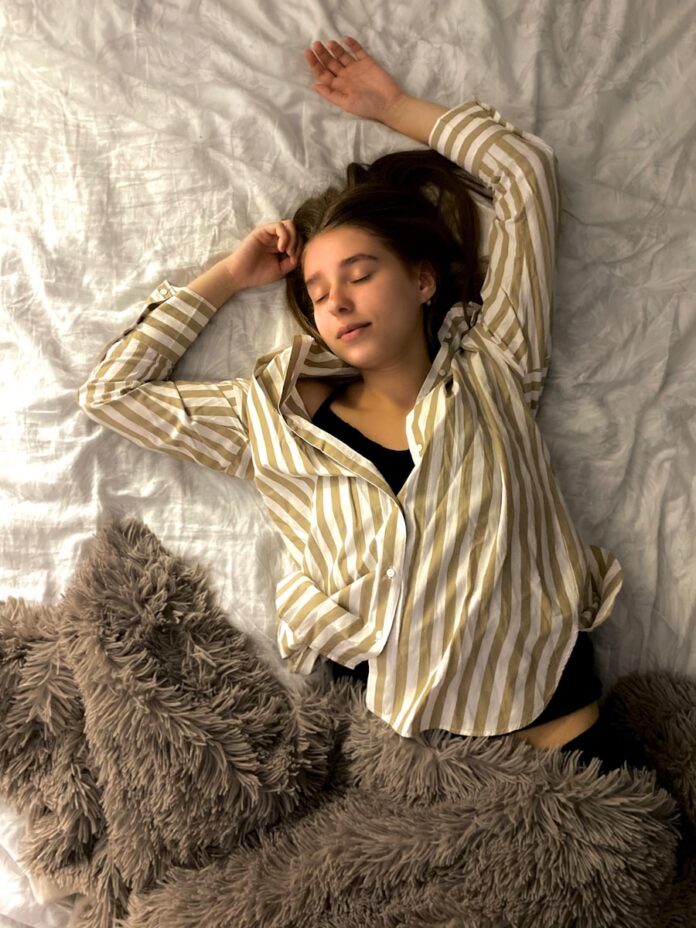 Photo by MILAN GAZIEV woman in white and black striped long sleeve shirt lying on bed